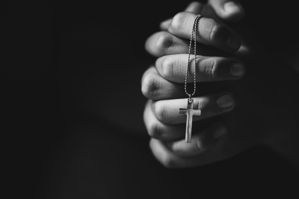 Close up christian hands holding cross while praying.